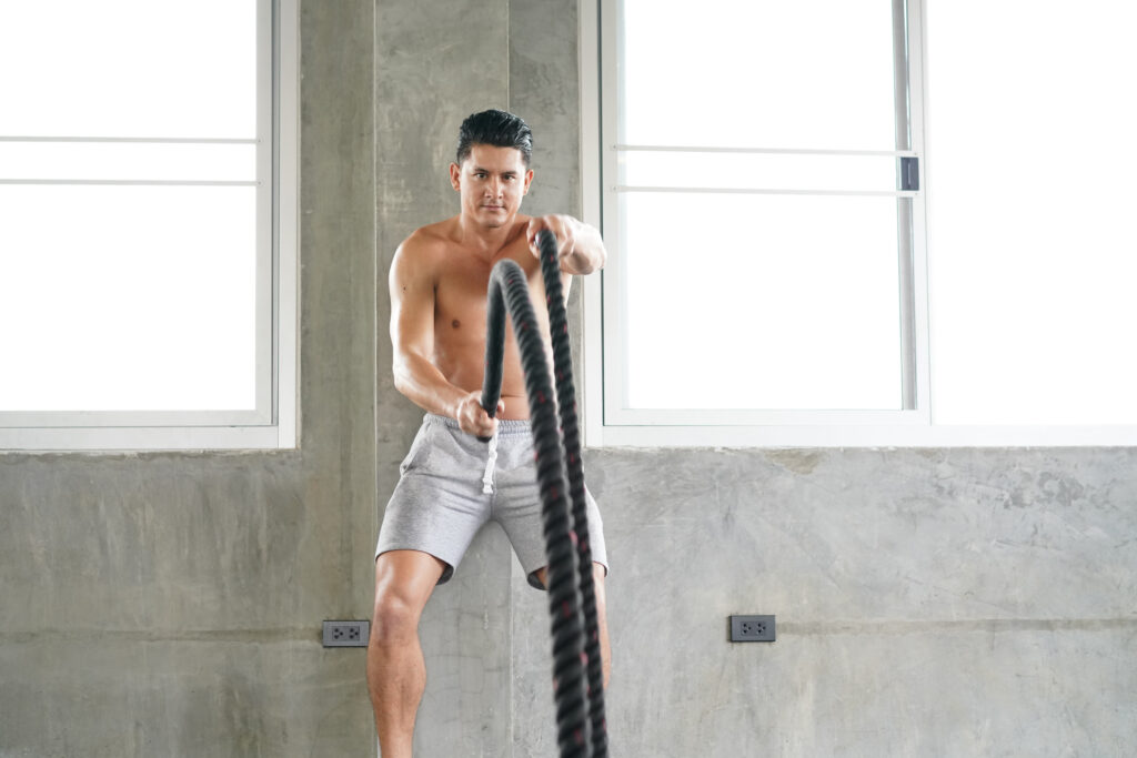 Athletic man with battle rope doing exercise in functional training fitness gym exercising with battle ropes at gym.