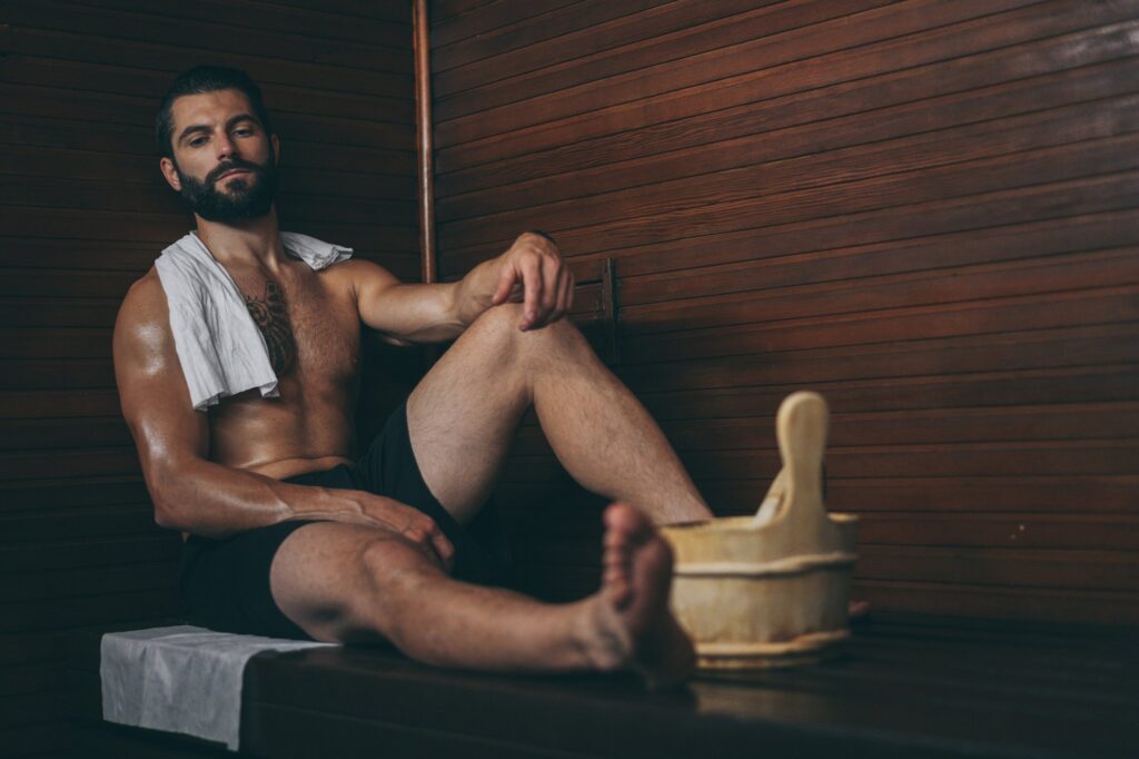 Sauna before or after workout: man relaxing with a towel in a wooden sauna after training